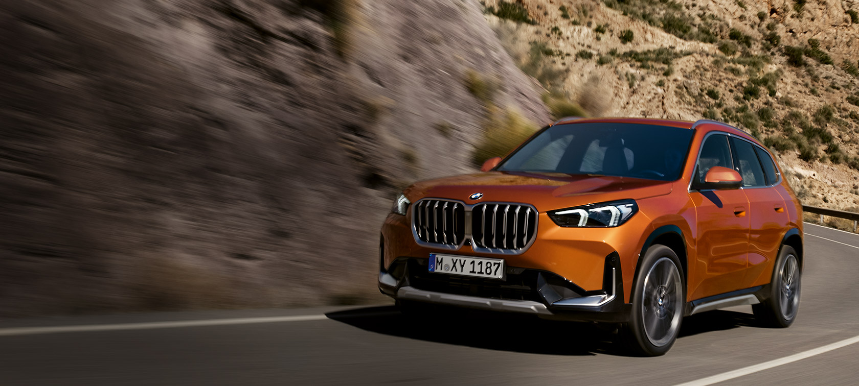 BMW X1 U11 xLine Utah orange metallic, vue de trois quarts avant sur route de campagne